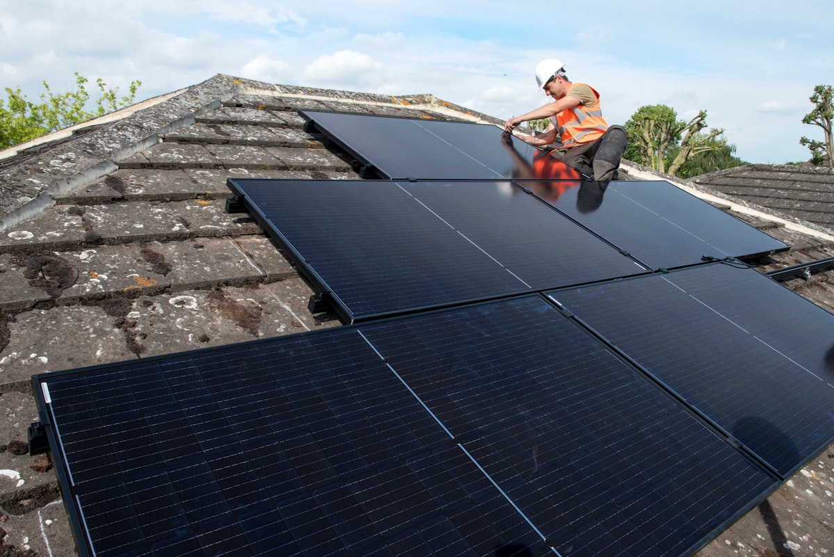 A male roofer installing solar panels on a house